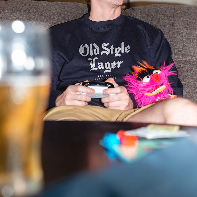 man sitting on couch with game controller in his hands wearing crewneck with "old style lager" on it
