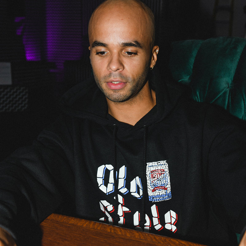 man sitting at a desk with hoodie on that has old style words and  beer on it 